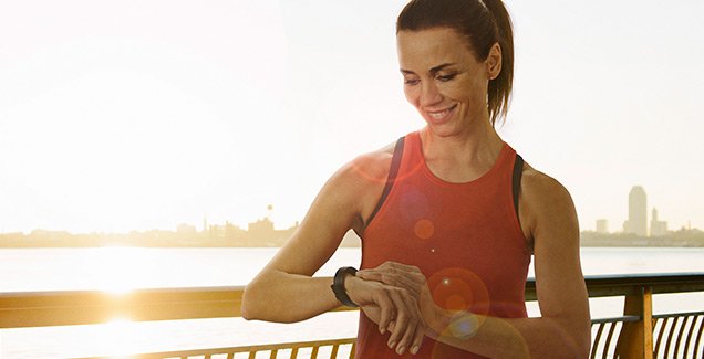 Slika privlačne mlade ženske v športnih oblačilih, ki si ogleduje Verovalov sledilec aktivnosti na svojem zapestju