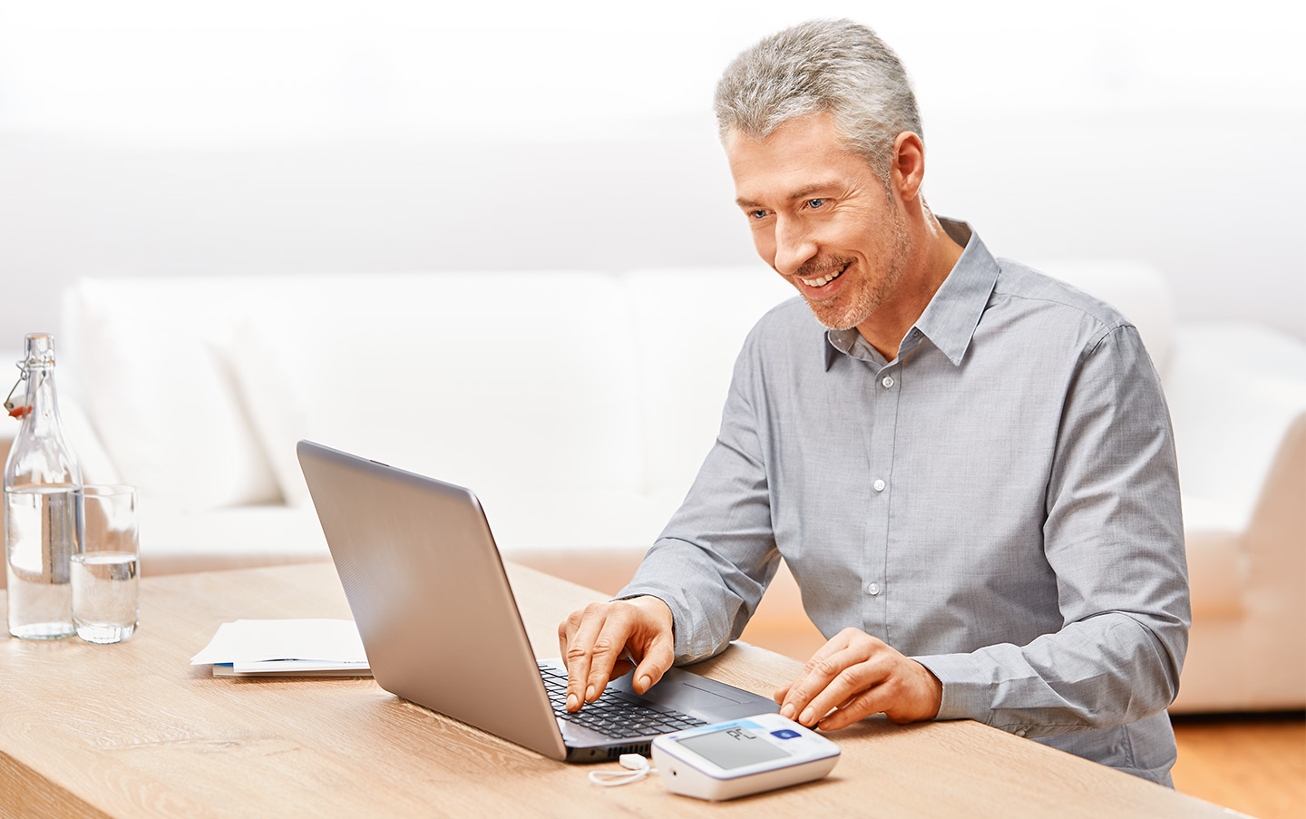 Obrázok šedovlasého usmievajúceho sa muža pri počítači pripojenom na jeho tlakomer Veroval®
