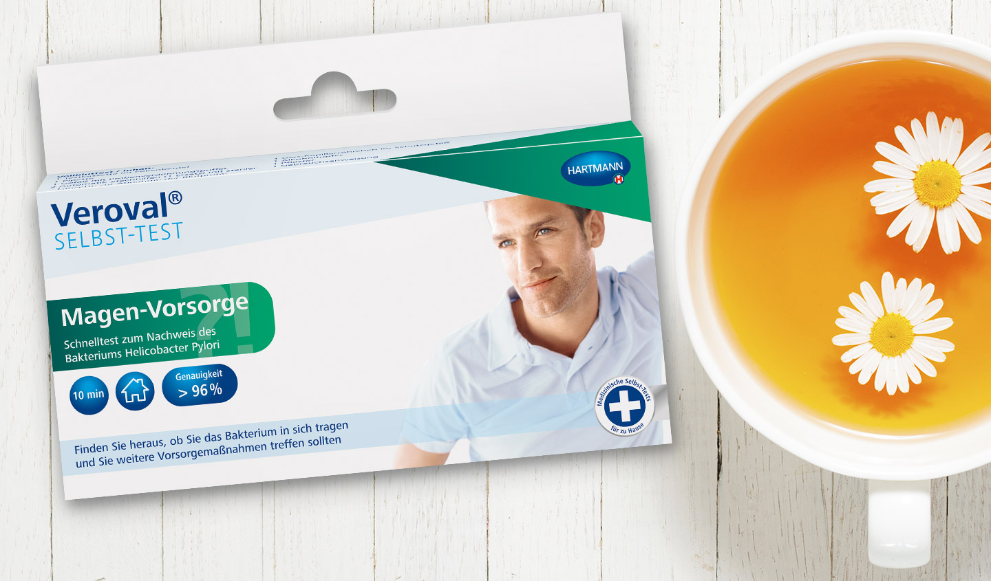 Eine Packung des Veroval® Selbst-Tests zur Magenvorsorge liegt auf einer weißer Holzoberfläche neben einer Tasse Tee.